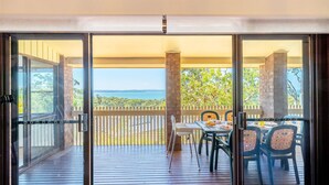 A balcony with a table and chairs, a view of the sea, and a wooden deck. - Casa Carinho, 24 Wallawa Rd - spectacular water views, pet friendly, air con and Wi-Fi (Nelson Bay)
