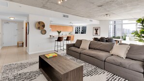 A modern living room with a sectional sofa, a coffee table, and a kitchen area in the background. - Amazing sunset view with Pool, 2b/2ba, gym , Best location A+! (Miami)