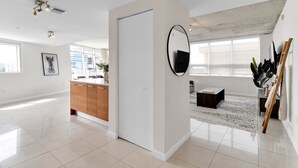 A spacious, modern living area with a large window, a flat-screen TV, a wooden cabinet, and a round mirror. - Amazing sunset view with Pool, 2b/2ba, gym , Best location A+! (Miami)