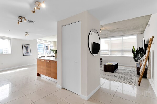 A spacious, modern living area with a large window, a flat-screen TV, a wooden cabinet, and a round mirror. - Amazing sunset view with Pool, 2b/2ba, gym , Best location A+! (Miami)
