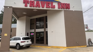 Entrada del hotel Travel Inn con fachada blanca, amplias ventanas y un estacionamiento con un SUV blanco.