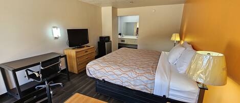 A hotel room with a bed, desk, chair, TV, microwave, and a lamp.