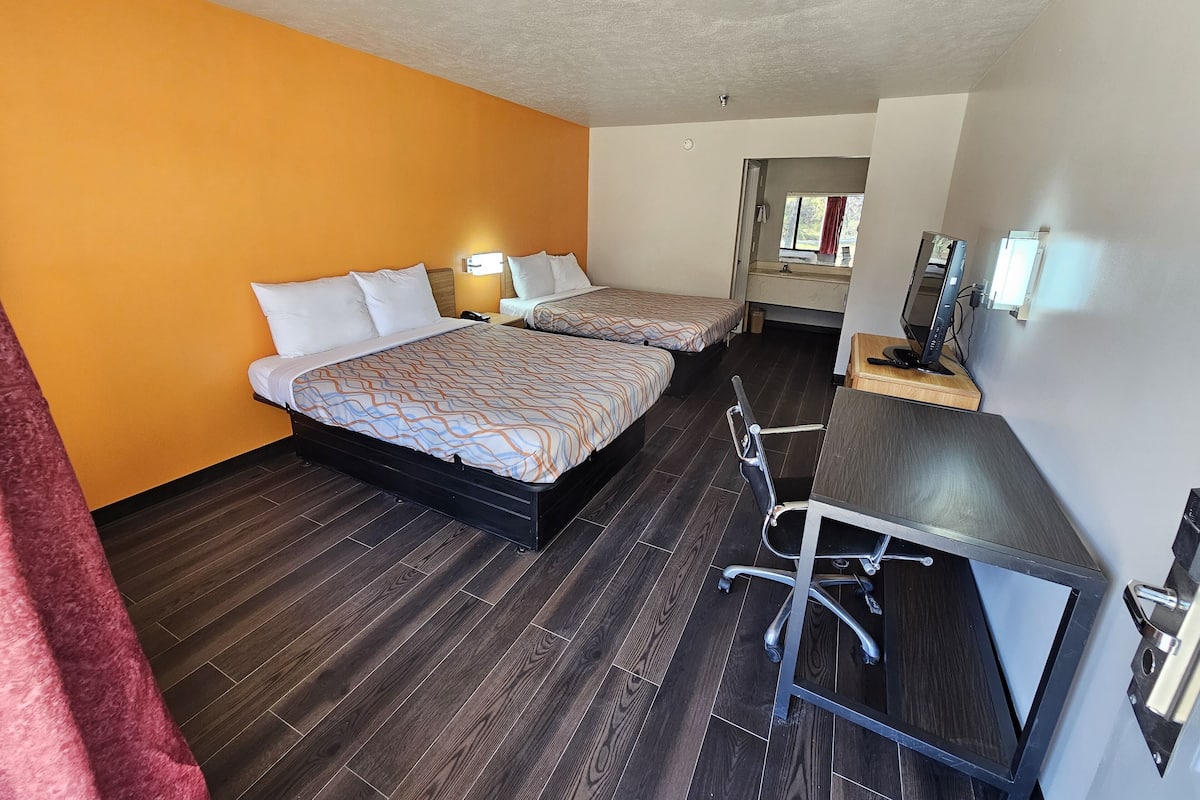 A hotel room with two beds, a desk, a chair, and a TV.