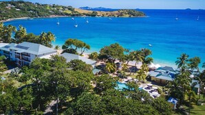 A resort with a pool area, palm trees, and a view of the ocean with boats.