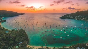 An aerial view of a coastal area with numerous boats anchored in the water, surrounded by lush greenery and a clear sky.