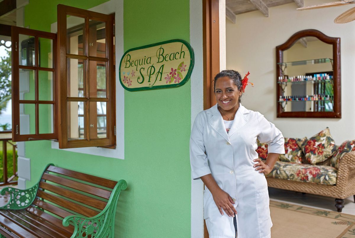 Uma pessoa vestindo uniforme branco ao lado de um letreiro que diz "Bequia Beach SPA".