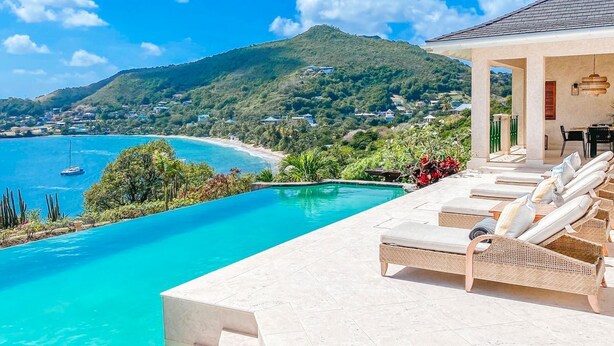 Un espace aménagé au bord de la piscine, avec des chaises longues, une vue sur l’océan et une montagne en arrière-plan.
