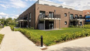 Un bâtiment moderne avec une façade en briques, deux balcons et un trottoir dallé.