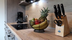 Une cuisine avec un plan de travail en bois, un panier de fruits, une machine à café et un bloc à couteaux.