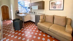 Eine kleine Küche mit Mikrowelle, Toaster und Spüle. Ein Sofa und ein kleiner Tisch mit einem Stuhl sind ebenfalls vorhanden. Ein gerahmtes Bild hängt an der Wand.