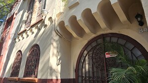 Ein Gebäude im traditionellen Baustil mit einem großen Bogenportal, schmiedeeisernen Verzierungen und einem Balkon mit Blumentöpfen.