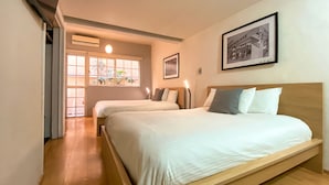 Ein Hotelzimmer mit zwei Betten, einem Fenster mit Pflanzen, einem gerahmten Bild und einem Holzboden.