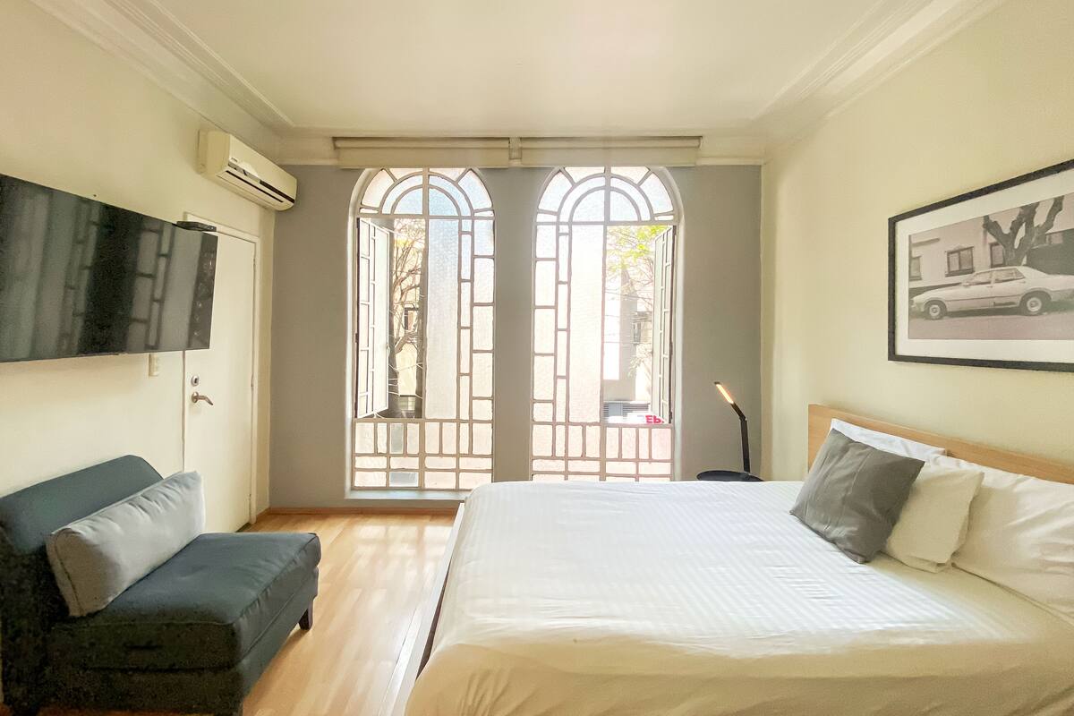 Een slaapkamer met een bed, een bank, een televisie en een raam met uitzicht.