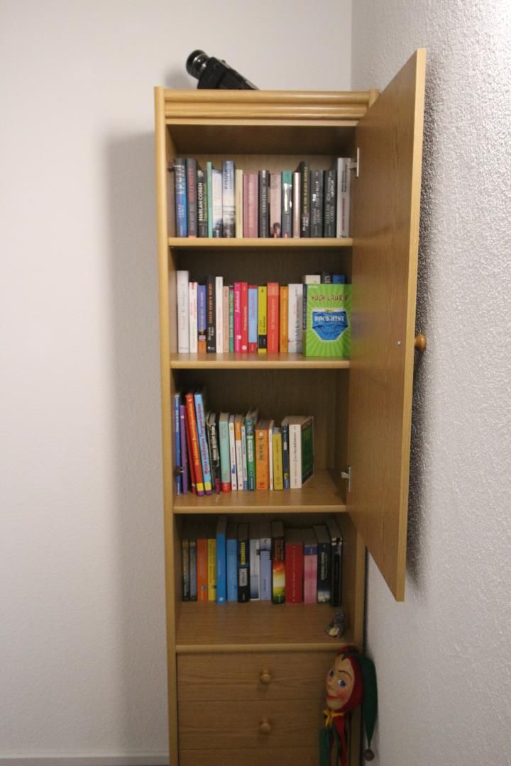 Ein Bücherregal aus Holz mit mehreren Ablagen, gefüllt mit Büchern und einer kleinen Figur.