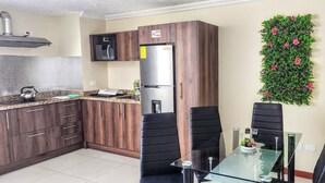 Eine moderne Küche mit dunklen Holzschränken, einem Edelstahlkühlschrank, einer Mikrowelle und einem Glastisch mit zwei schwarzen Stühlen.