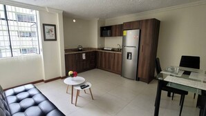 Eine moderne Küche mit dunklen Holzschränken, einem Edelstahlkühlschrank und einer Granitarbeitsplatte. Ein kleiner runder Tisch steht dort mit einer Blumenvase und einer Fernbedienung.