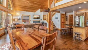 Un vaste espace de vie comprenant une grande table à manger en bois, un coin salon confortable et une cuisine dotée de meubles en bois et d’un bar.
