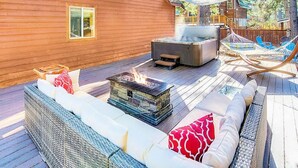 Une terrasse en bois avec un foyer en pierre, des sièges d’extérieur et un jacuzzi.