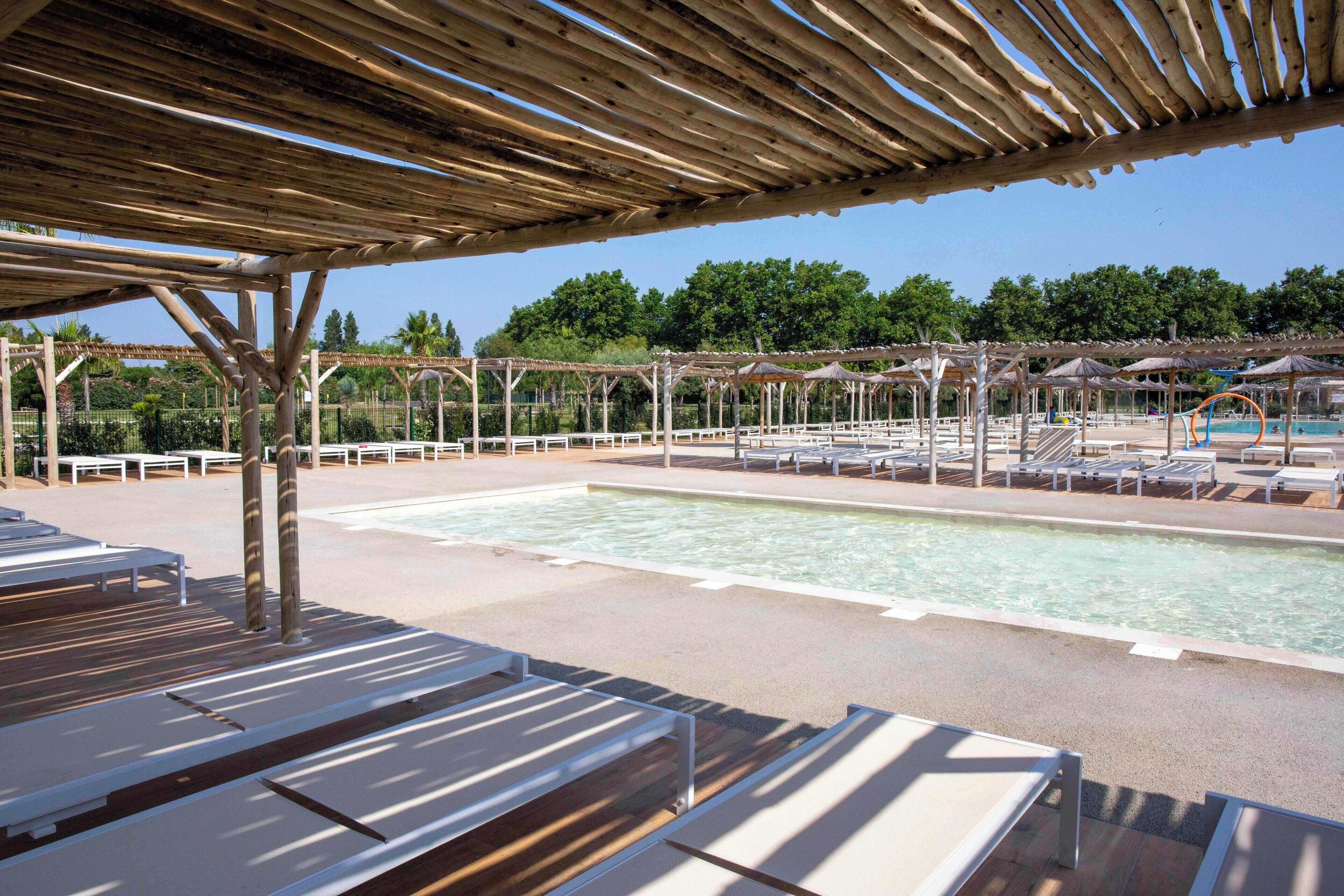 Un espace piscine avec des chaises longues et un coin salon abrité.