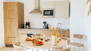 Une cuisine moderne avec des meubles en bois, un four à micro-ondes et un coin repas agrémenté de chaises en osier et d’une table ronde préparée pour le petit-déjeuner.