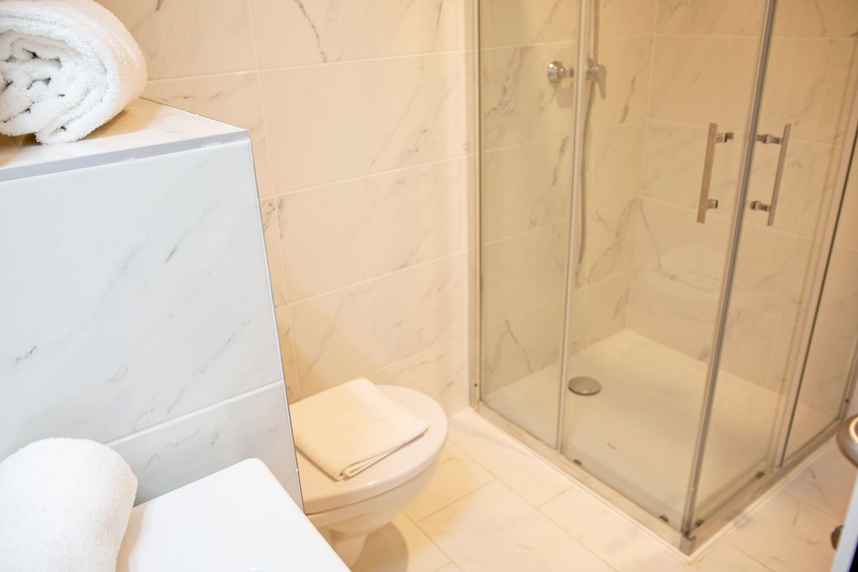 A bathroom with a toilet, a glass-enclosed shower, and a marble-tiled wall.