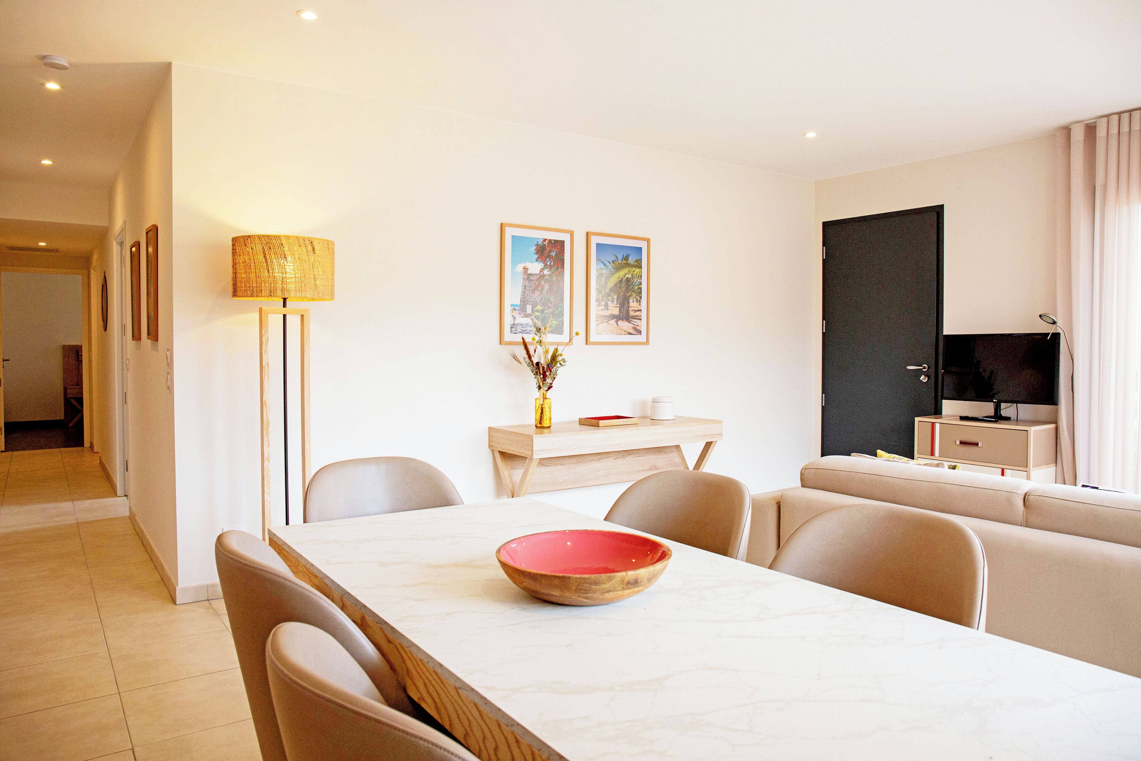 A modern hotel room with a dining area, a sofa, a TV, and framed pictures on the wall.