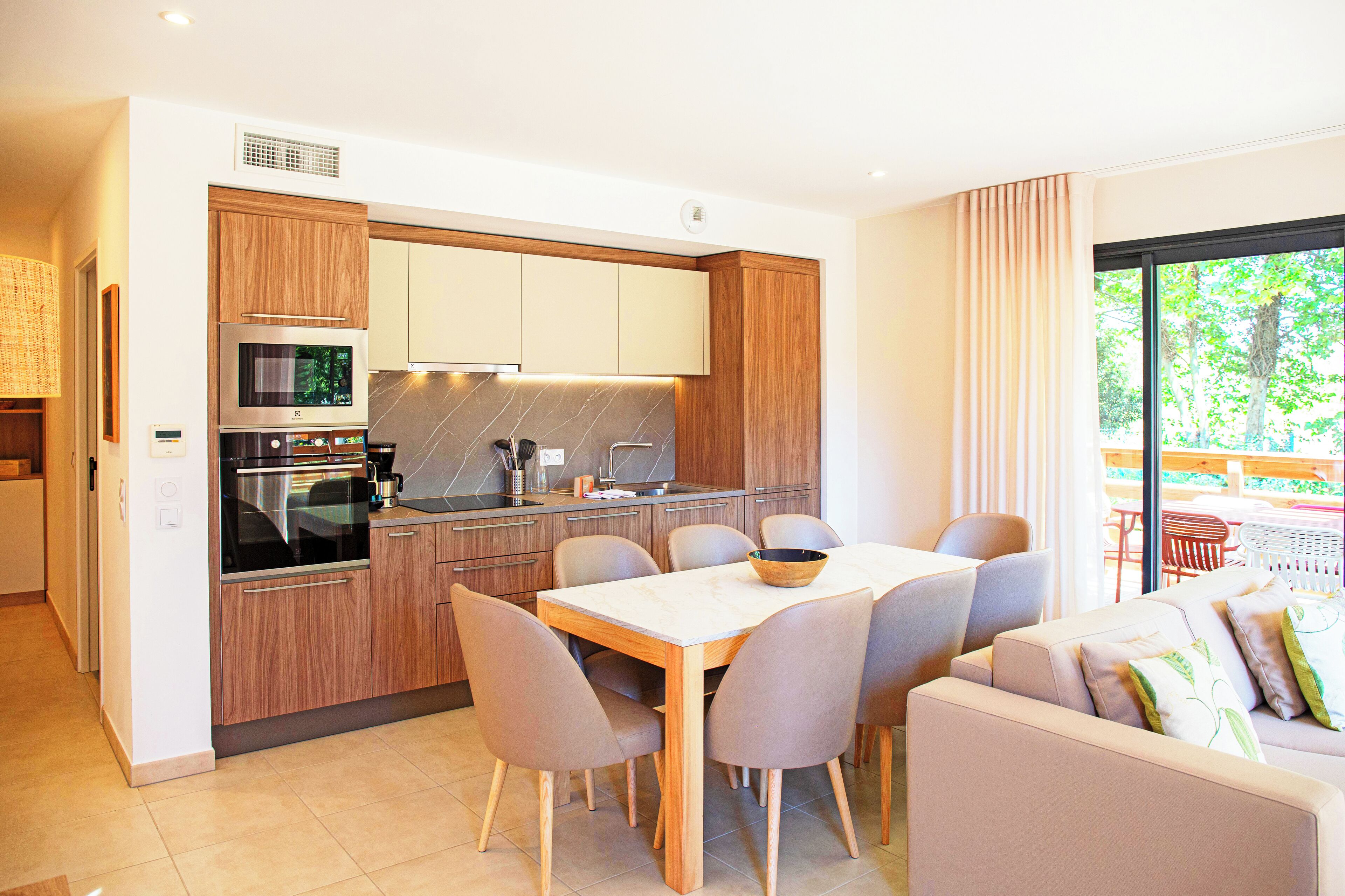 A modern kitchen with wooden cabinets, a built-in oven, and a dining area with a table and chairs.