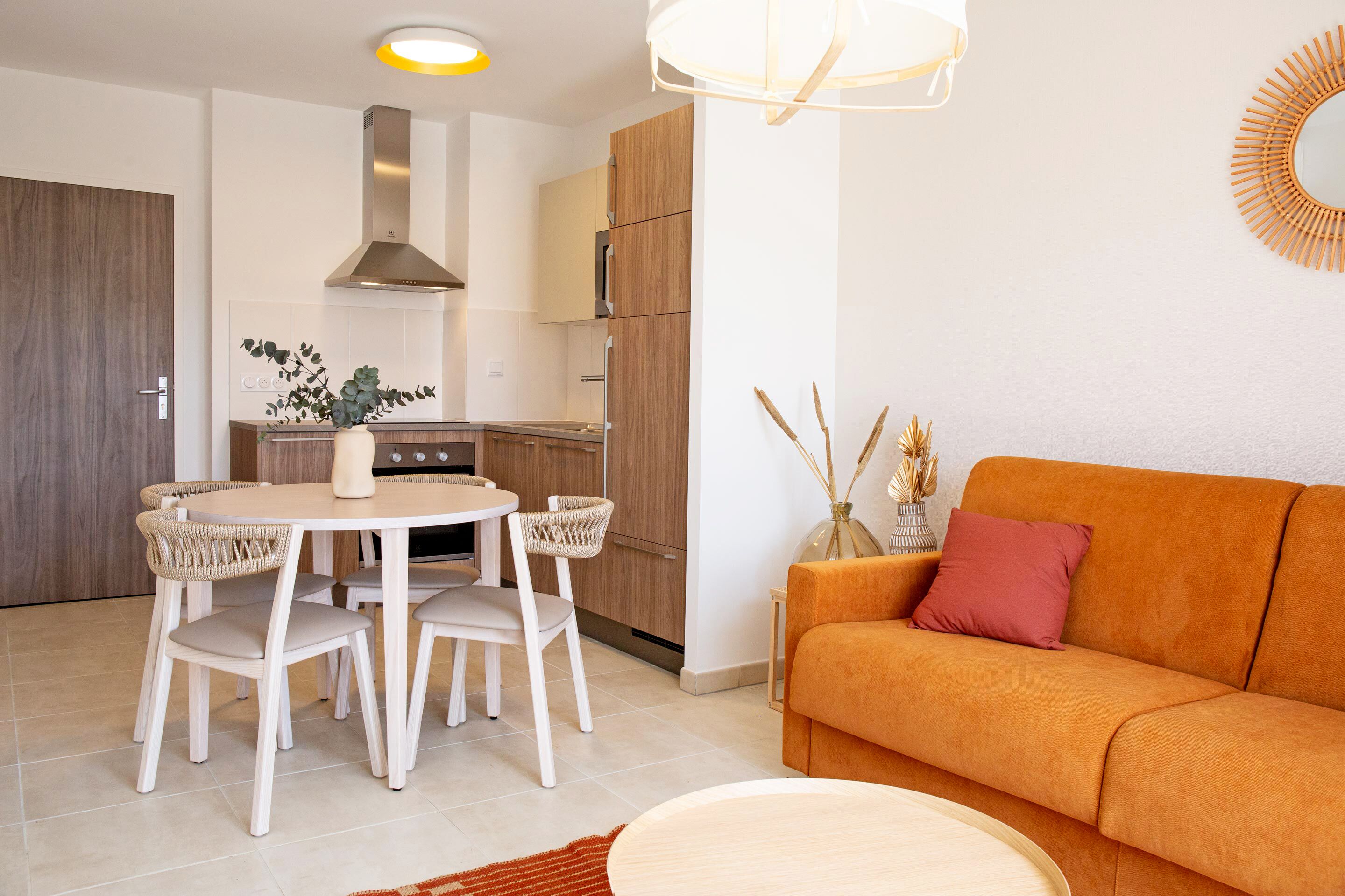 A modern kitchen with wooden cabinets, a built-in stove, and a dining area with a round table and chairs.