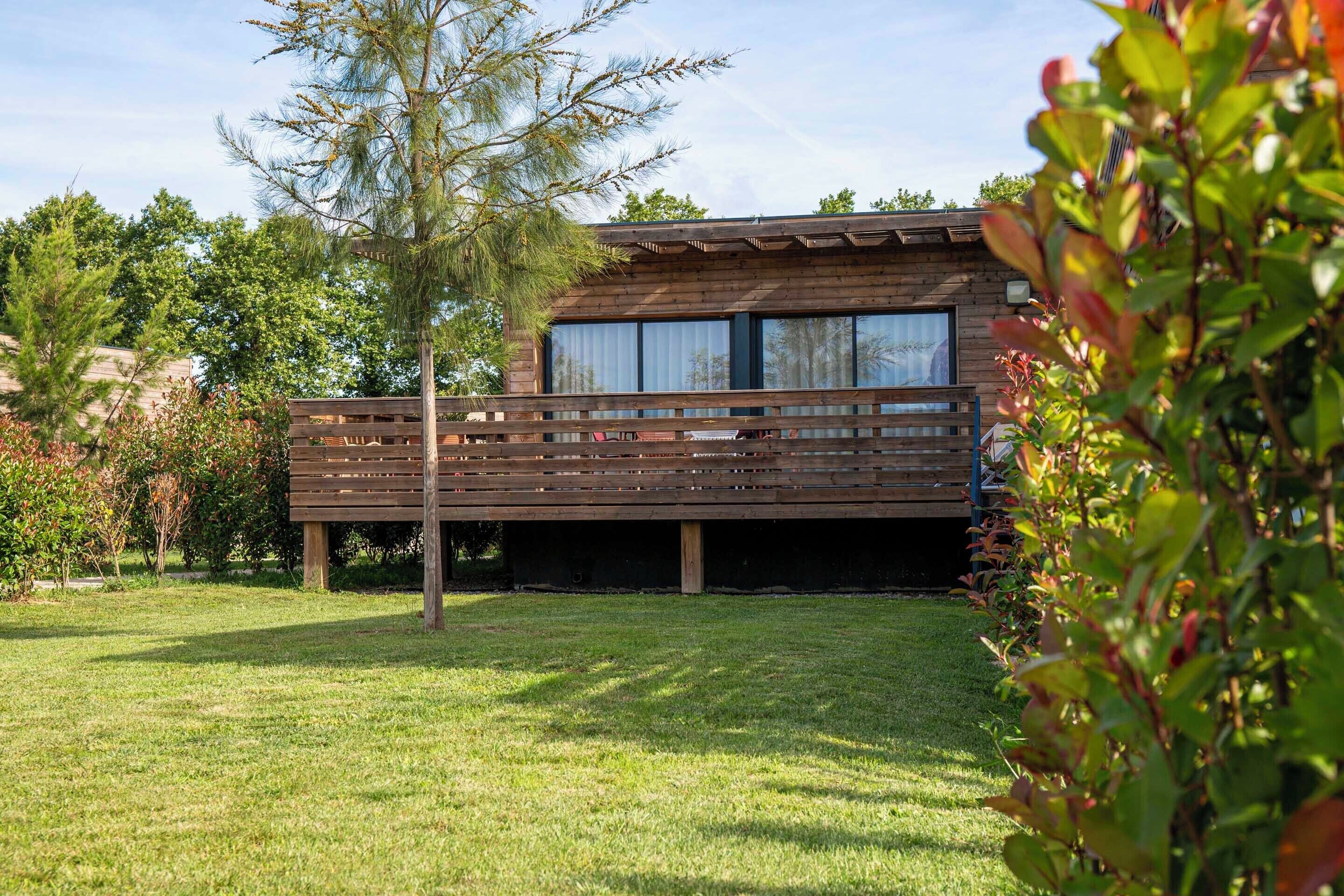 Eine Holzhütte mit einer Terrasse, umgeben von einem Rasen und Bäumen.