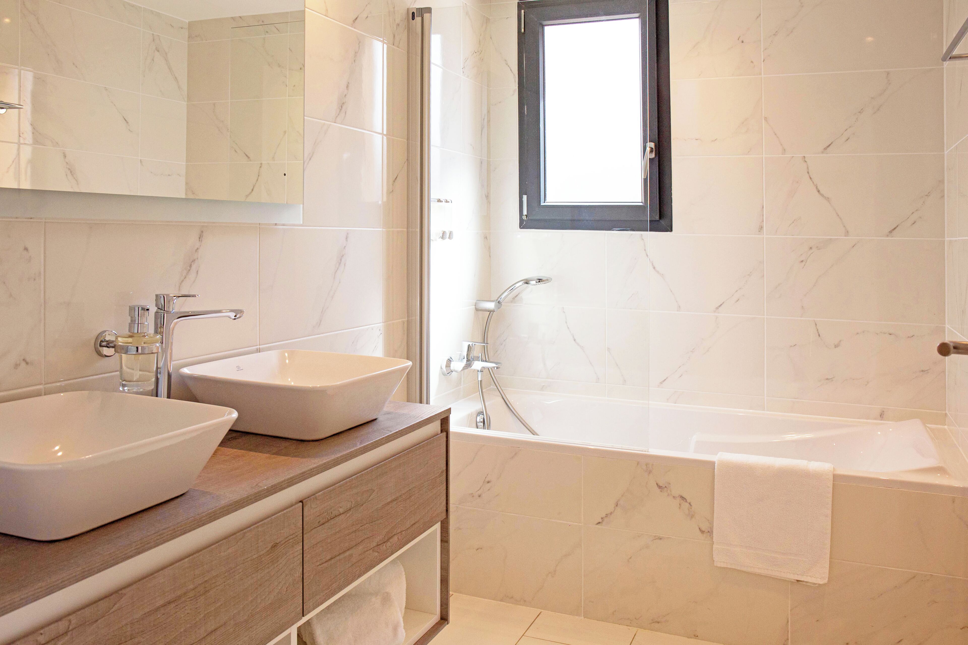 Un baño moderno con dos lavamanos sobre encimera, una bañera y un ventanal.