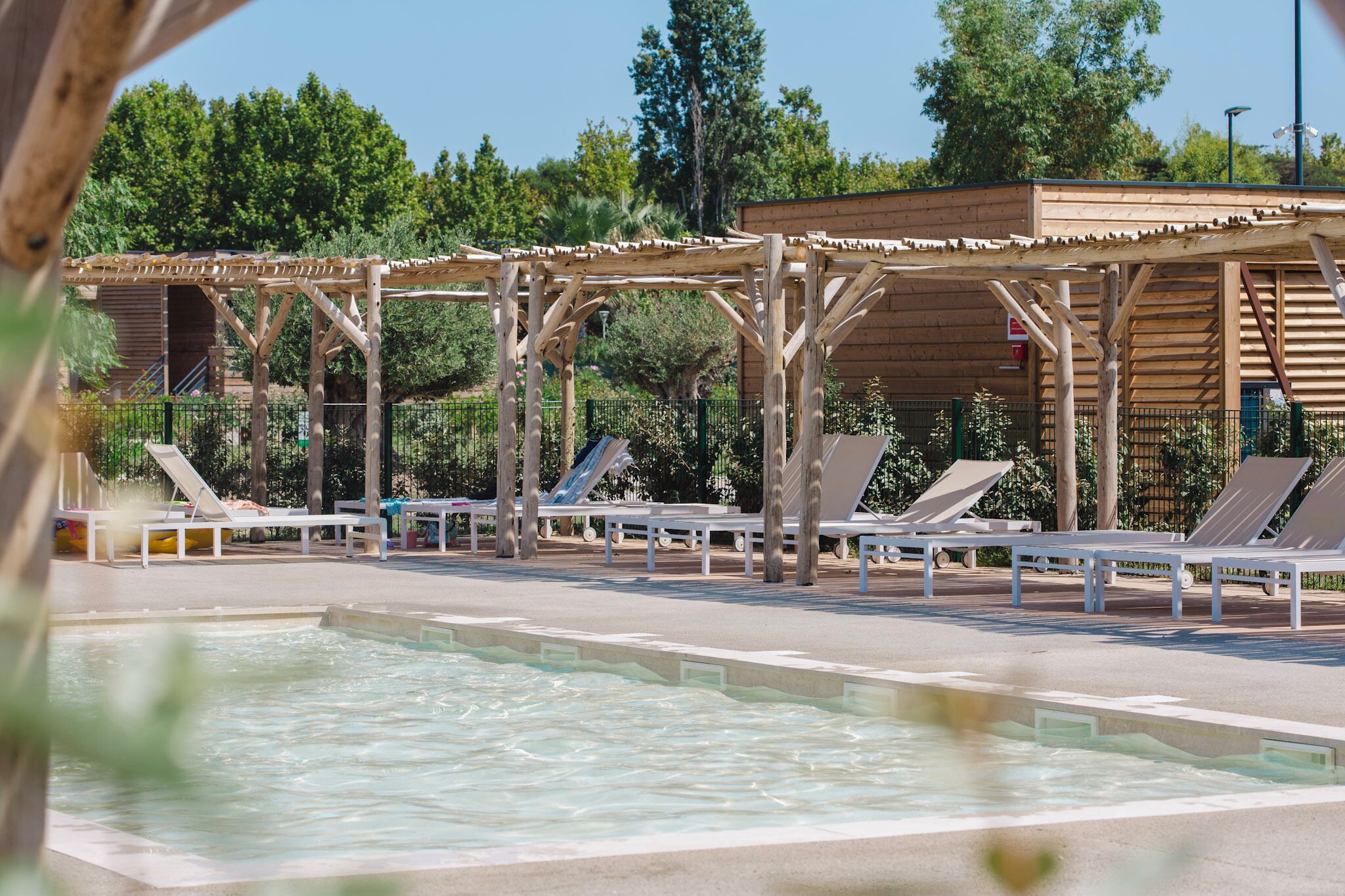 Zona de piscina con sillas de descanso y una estructura de pérgola de madera.
