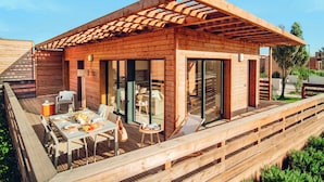 Une cabane moderne en bois, dotée d’une terrasse, de meubles d’extérieur et de grandes portes-fenêtres coulissantes.