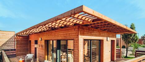 A modern wooden cabin with a deck, outdoor seating, and large sliding glass doors.