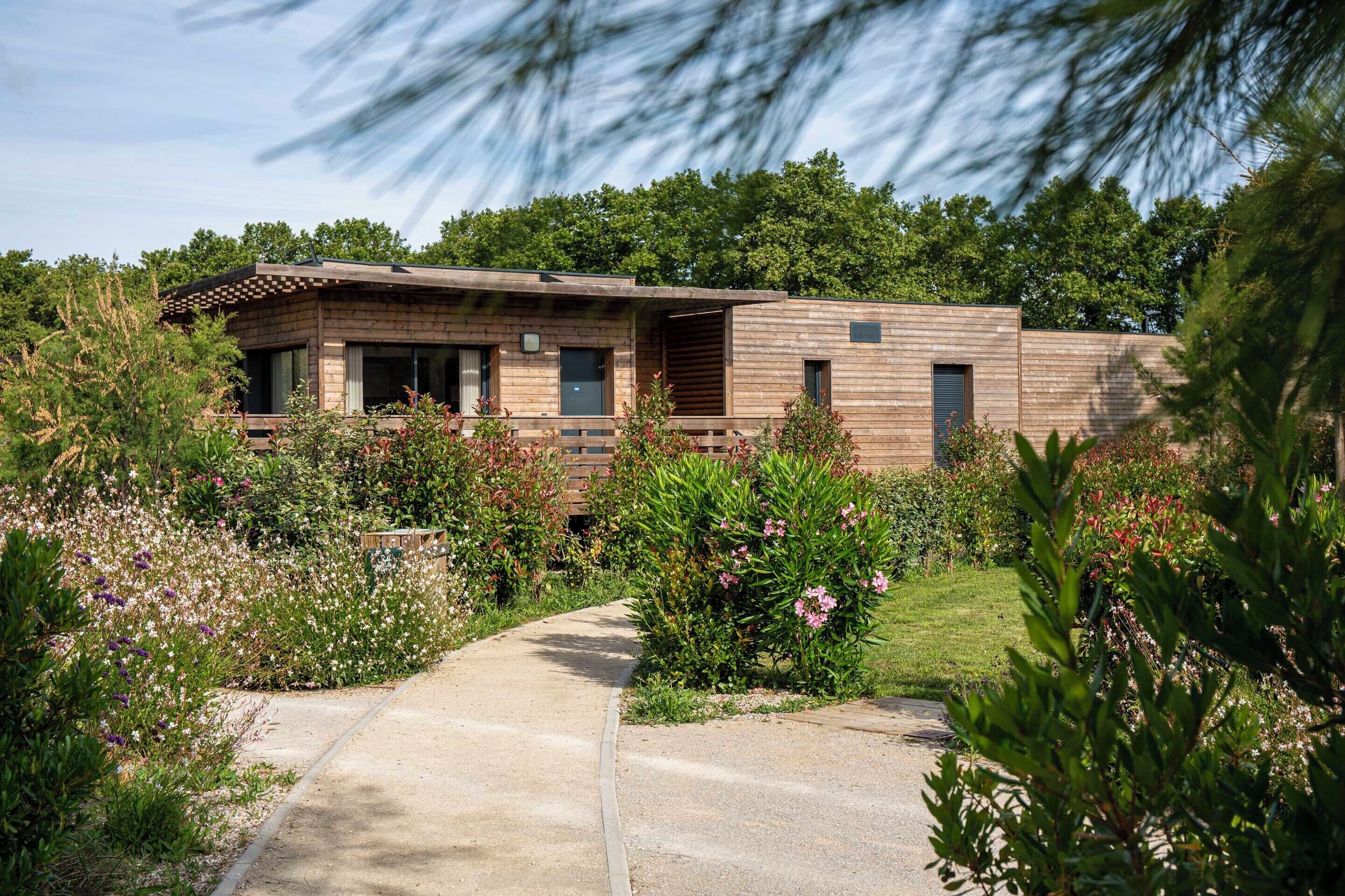Una casa moderna con fachada de madera, un camino de entrada pavimentado y un jardín con diversas plantas y flores.