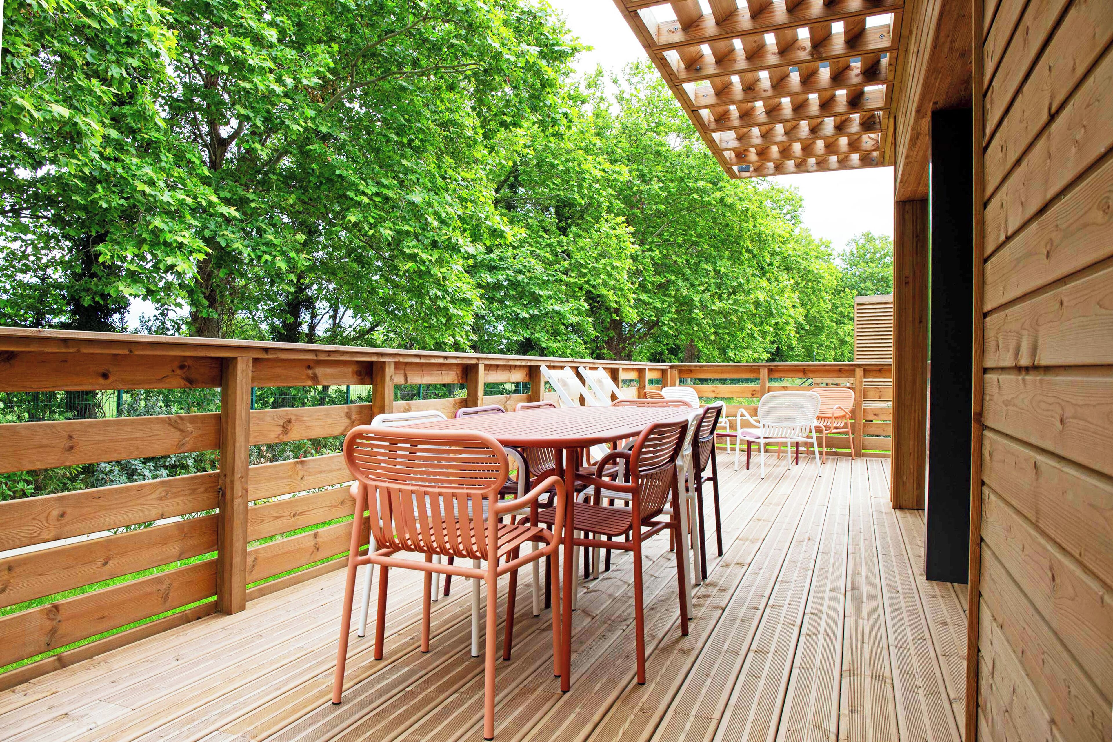 Una terraza de madera con una mesa y sillas, rodeada de un cerco de madera y árboles.