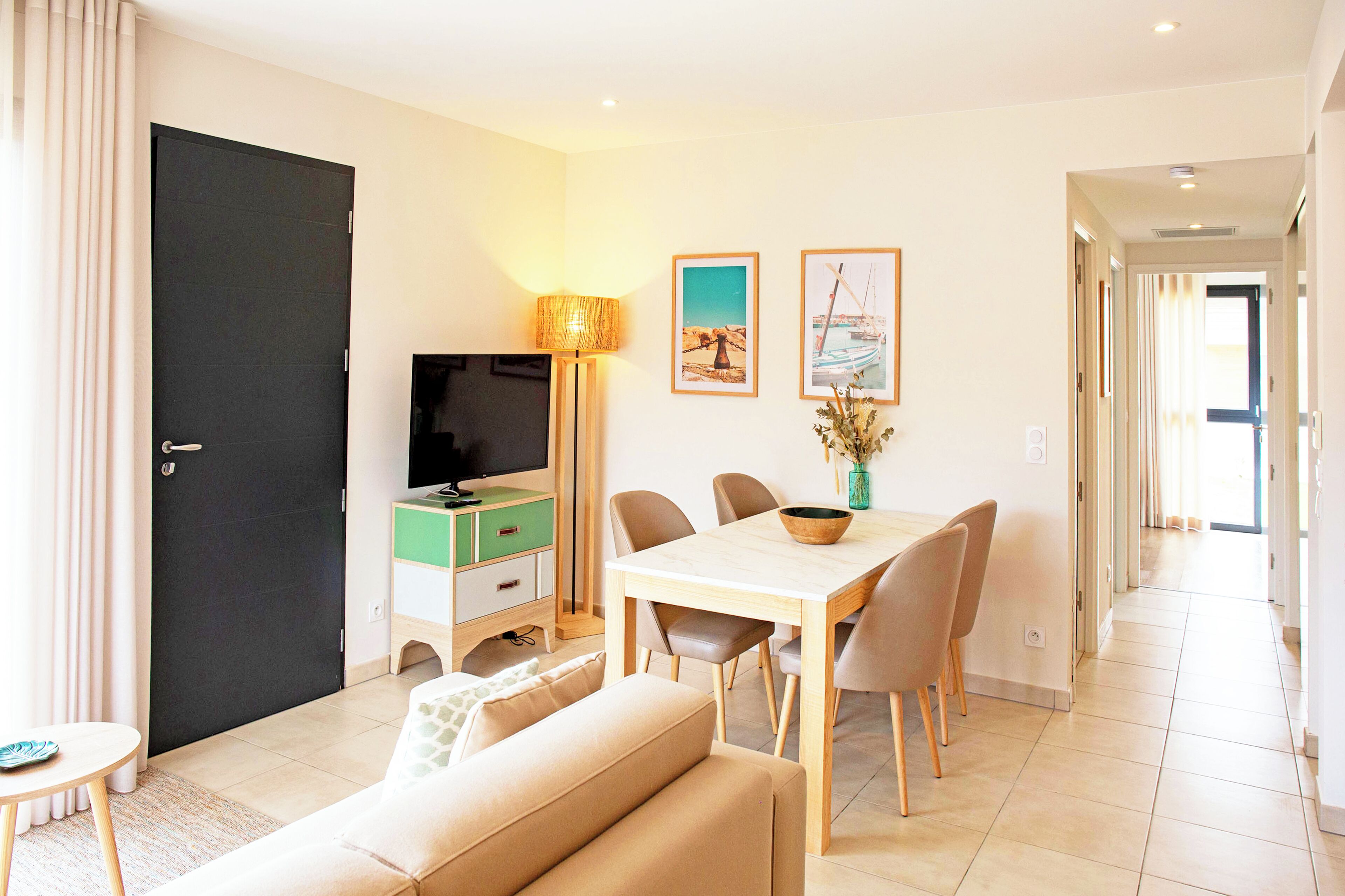 Un salon moderne comprenant un canapé, une table à manger avec des chaises, un téléviseur et une lampe.