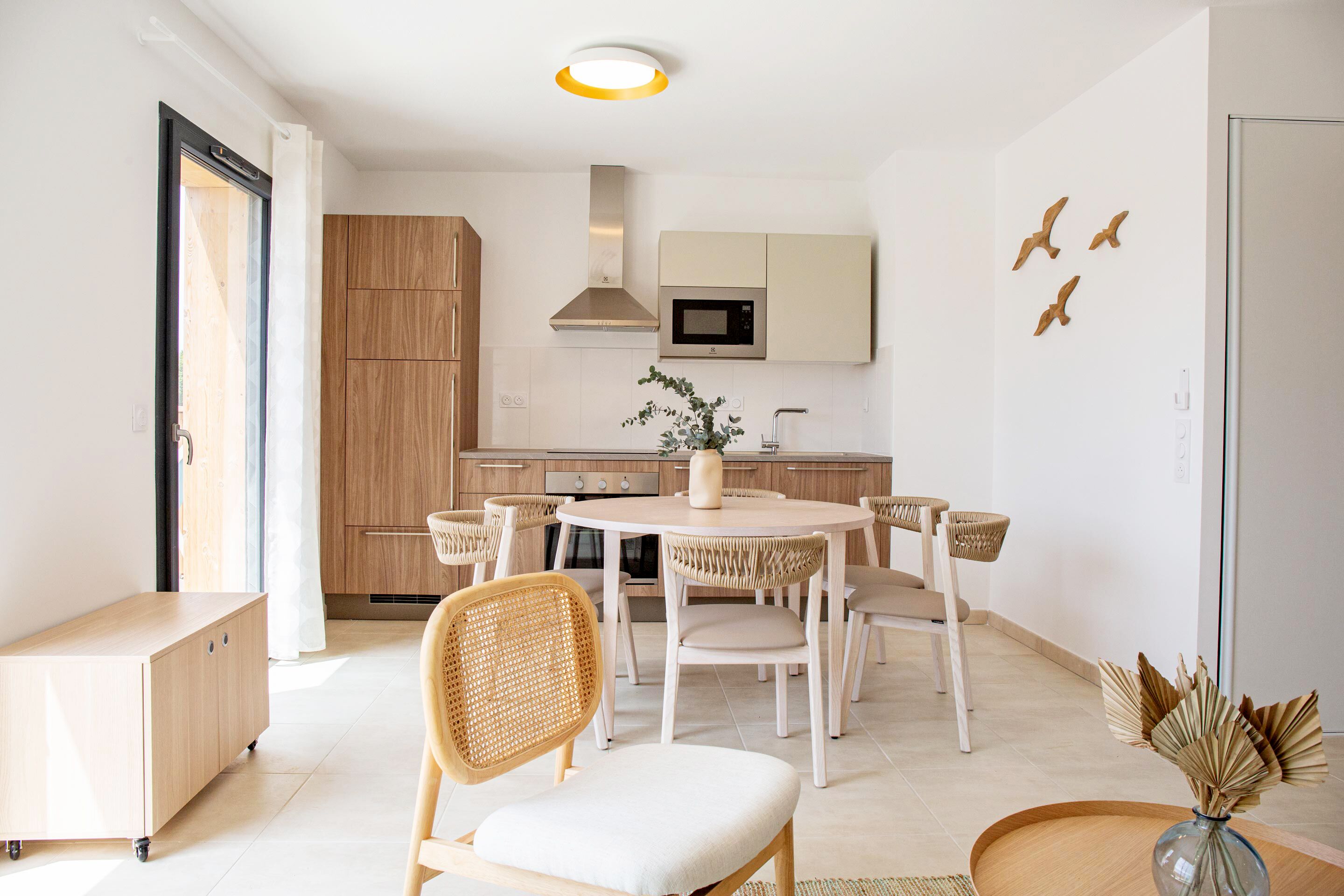 A modern kitchen with wooden cabinets, a round dining table, and wicker chairs.
