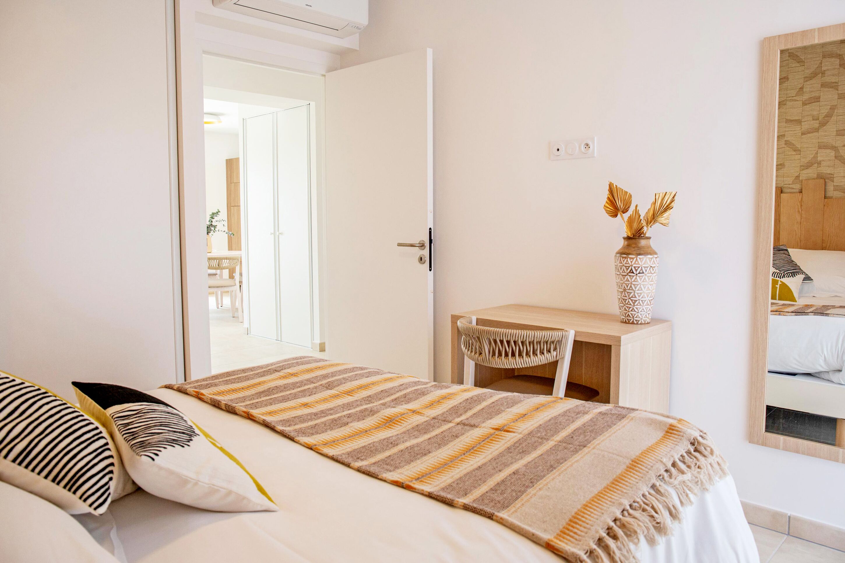 A bedroom with a bed, a desk, and a chair. There is a door leading to another room.