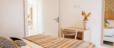 A bedroom with a bed, a desk, and a chair. There is a door leading to another room.