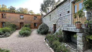 A courtyard with a gravel path, wooden and stone buildings, and potted plants. - Barraconu (Porto-Vecchio)