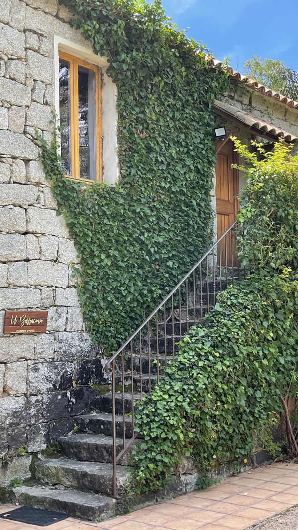 A stone building with a wooden staircase and a sign reading "W. Zabracou". - Barraconu (Porto-Vecchio)