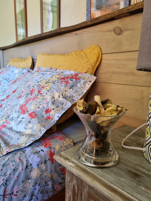 A bed with floral bedding, a wooden headboard, and a bedside table with a glass vase containing dried flowers. - Barraconu (Porto-Vecchio)