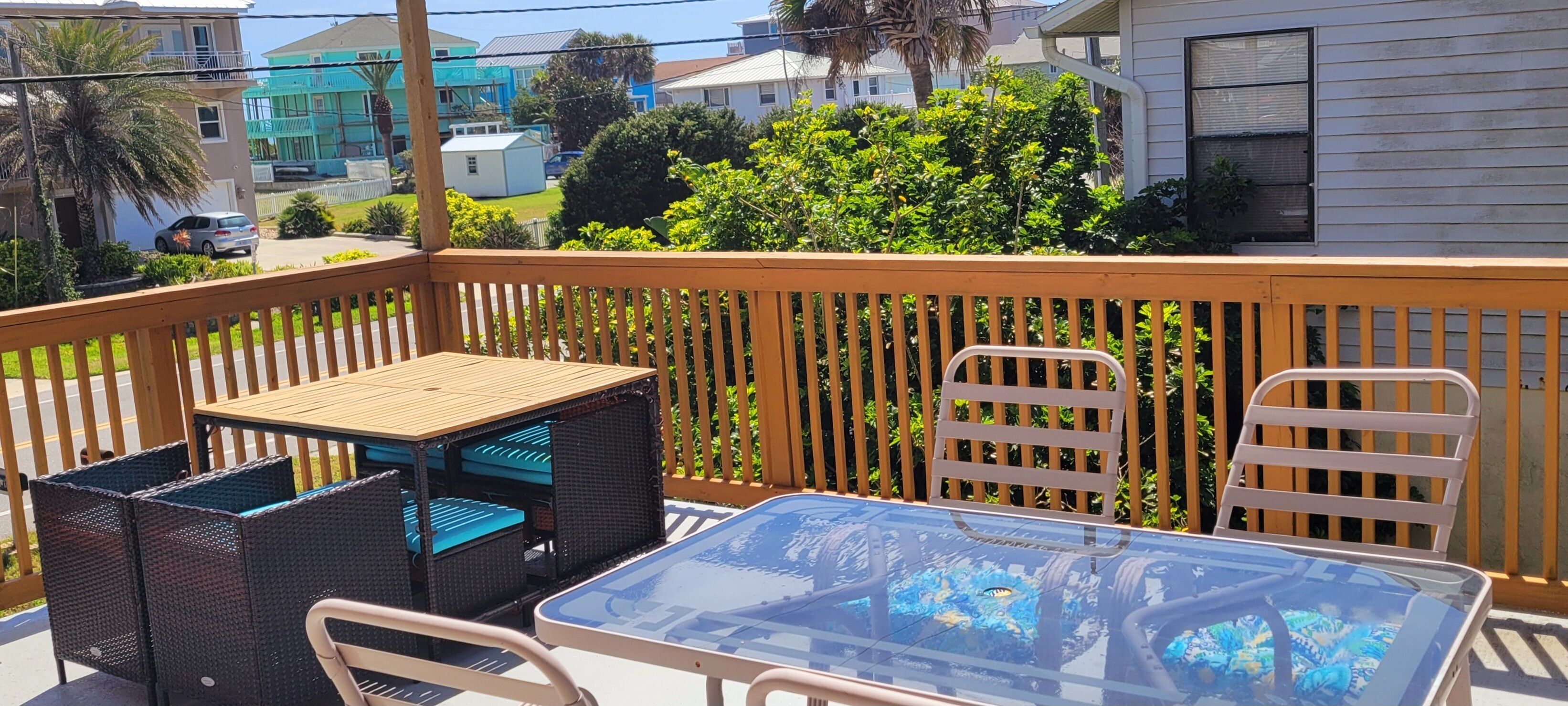 A balcony with a glass table, wicker chairs, and a wooden table.