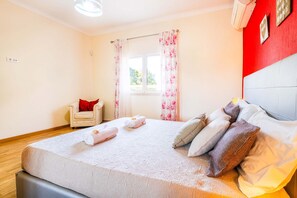Een slaapkamer met een bed, kussens, een stoel, een raam met gordijnen en een rode muur.