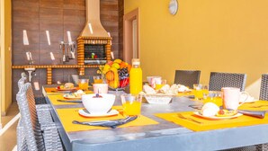 A dining area with a brick oven, yellow walls, and a long table set for breakfast. - Villa w/ Heatable Pool and Jacuzzi in Carvoeiro (Carvoeiro)