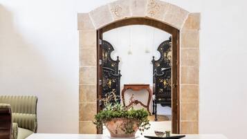 Um quarto com uma mesa branca, uma planta em vaso e vista através de uma porta arqueada para um quarto preto e dourado com uma cadeira e uma pequena mesa.