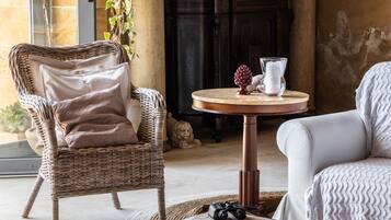 A wicker chair with a cushion, a round table with a vase and a decorative item, and a sofa with a patterned cover.