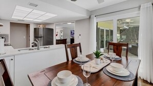 Een moderne keuken met een eethoek, grote ramen en een plafondventilator.
