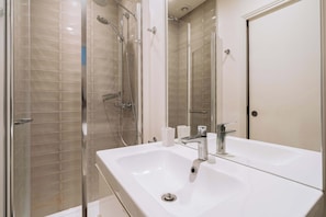 A modern bathroom with a glass-enclosed shower, a double sink, and a large mirror.