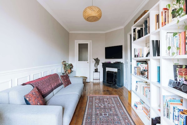 A living room with a sofa, a fireplace, a bookshelf, and a television.